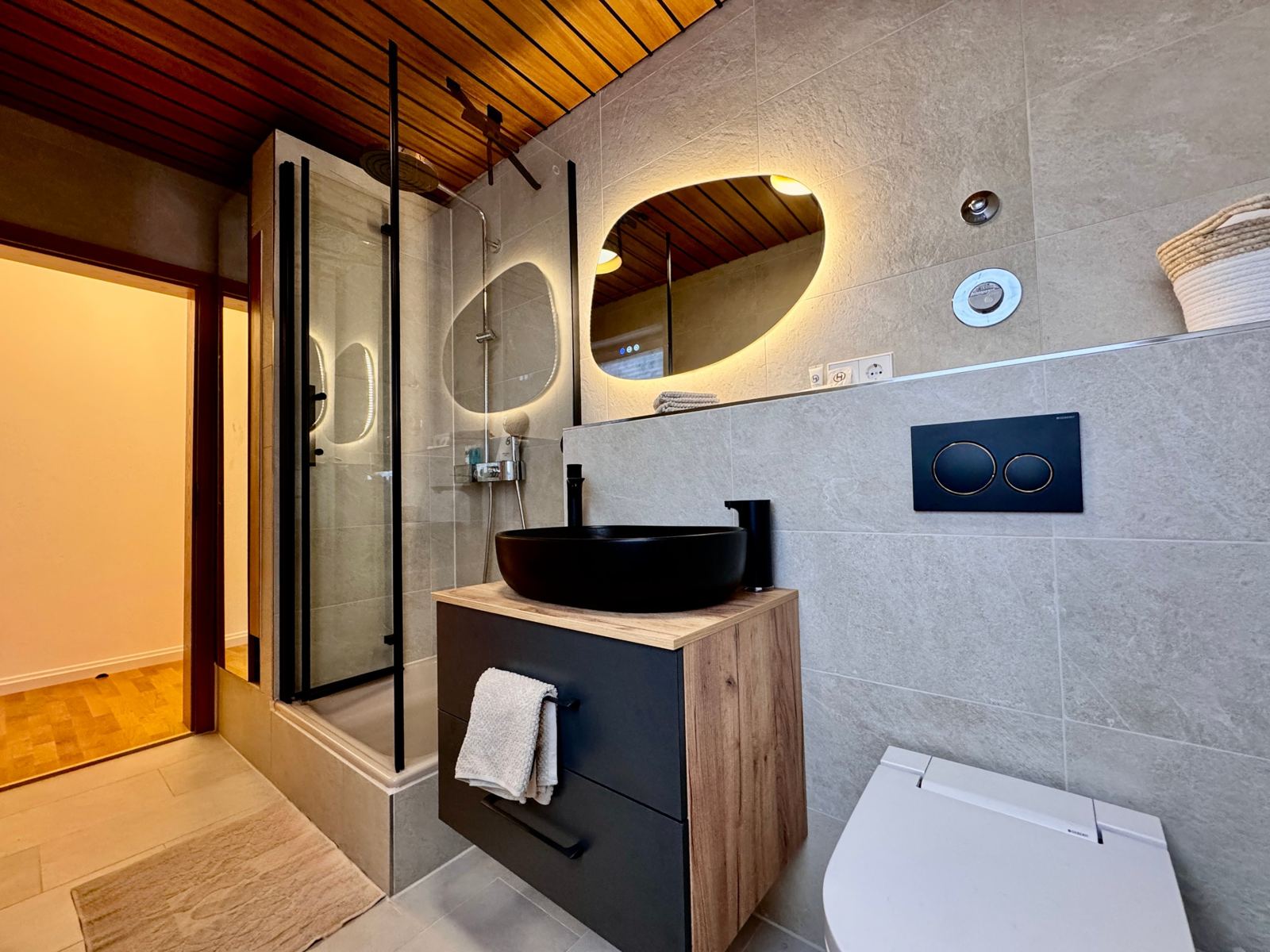 Badezimmer mit Waschbecken, beleuchtetem Spiegel und Holzdecke